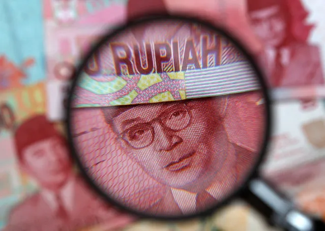 One hundred thousand rupiah notes are seen through a magnifying glass in this picture illustration, March 14, 2013. (Photo by Edgar Su/Reuters)