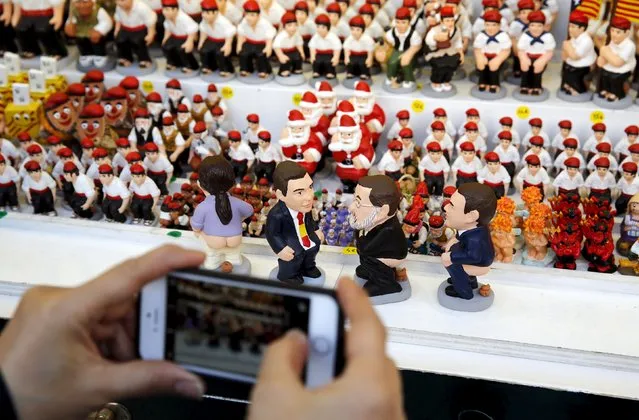 A woman takes a picture with her mobile phone of clay "caganers" representing Spanish Prime Minister Mariano Rajoy (2nd R), Podemos's candidate Pablo Iglesias (L), Socialist Party (PSOE) leader Pedro Sanchez (2nd L) and Ciudadanos party leader Albert Rivera (R) on display at the Santa Llucia Christmas market in central Barcelona, Spain, December 16, 2015. (Photo by Albert Gea/Reuters)