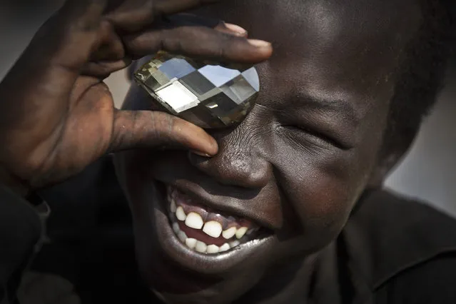 A displaced boy mimics the photographer taking a picture of him, using a fake plastic jewel, at a United Nations compound which has become home to thousands of people displaced by the recent fighting, in the capital Juba, South Sudan Sunday, December 29, 2013. (Photo by Ben Curtis/AP Photo)