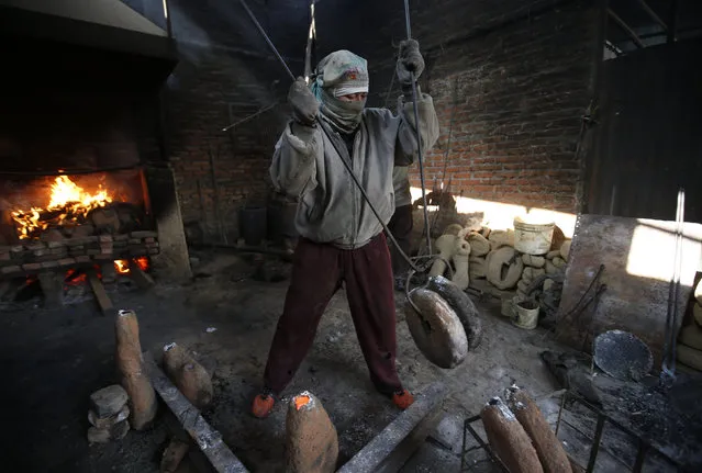 A worker carries moulds filled with melted copper as he makes statues in Lalitpur, Nepal December 23, 2015. (Photo by Navesh Chitrakar/Reuters)