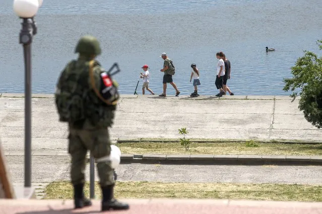 A picture taken during a media tour organized by the Russian Army shows a Russian serviceman standing guard as a family walks on a promenade along the Dnipro River in Kherson, Ukraine, 20 May 2022. The Russian-appointed head of Ukraine's Kherson region, Volodymyr Saldo, said that the area will ‘soon become part of the Russian Federation’. The governor was installed by Russian forces after they took control of the southern Ukrainian region in March 2022. (Photo by Sergei Ilnitsky/EPA/EFE)