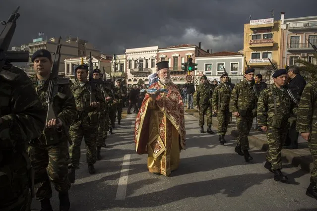 An Orthodox priest holds a cross as he is accompanied by a guard of honour during an Epiphany ceremony to bless the water in Mytilene port on the northeastern Greek island of Lesbos, Wednesday, January 6, 2016. Similar ceremonies to mark Epiphany Day were held across Greece at the sea, rivers, lakes and dams. An Orthodox priest throws a cross into the water and the swimmers race to retrieve it first. (Photo by Santi Palacios/AP Photo)