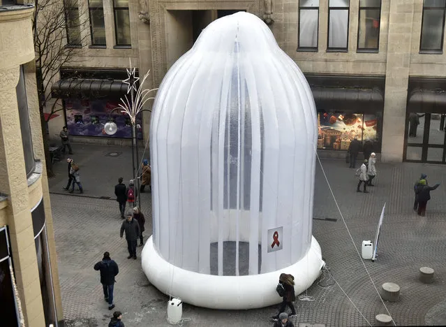 A people pass a giant condom that promotes safer s*x on a pedestrian street in Cologne, Germany prior the World AIDS Day, Wednesday, November 30, 2016. The World AIDS Day is held every First of December since 1988. (Photo by Martin Meissner/AP Photo)