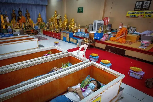 Buddhist devotees lie inside coffins as Buddhist monks officiate a “live funeral” ritual at Bangna Nai temple in Bangkok, Thailand, 13 February 2021 (issued 14 April 2021). A Thai Buddhist temple on the outskirts of Bangkok, officiates daily “live funerals” where Thai devotees lie inside coffins hoping to rid themselves of bad luck and attract good fortune. People choose to take part in the ritual following the recommendation of a fortune teller, looking to start anew. During the ceremony, devotees recite a prayer before lying inside a coffin, holding a flower while they are covered with a blanket. The belief is that through a symbolic death, they will rise up cleansed from their bad karma and be reborn anew. (Photo by Diego Azubel/EPA/EFE)