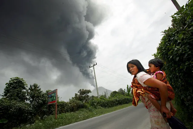 A woman and her daughter flee their home as Mount Sinabung erupts in Karo, North Sumatra, Indonesia, Tuesday, September 17, 2013. (Photo by Binsar Bakkara/AP Photo)
