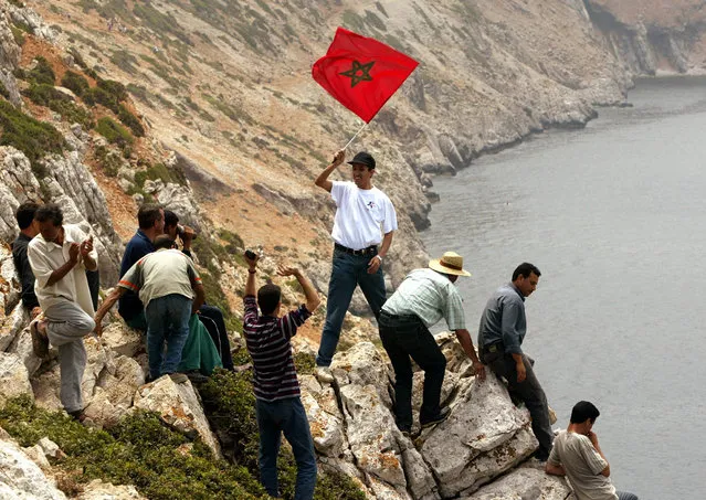 Moroccans cheer on a cliff as a man disembarks carrying a Moroccan flag on the disputed Perejil Islet off Morocco's Mediterranean coast, July 2002. (Photo by Desmond Boylan/Reuters)