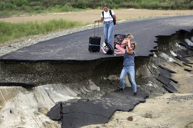 Tourists walk try to walk along a road damaged by flooding near the village of Tsybanobalka, Krasnodar region, Russia, Saturday, August 14, 2021. Heavy rains have flooded broad areas in southern Russia, forcing the evacuation of more than 1,,500 people. Authorities in the Krasnodar region said Saturday that more than 1,400 houses have been flooded following storms and heavy rains that swept the area this week. (Photo by AP Photo/Stringer)
