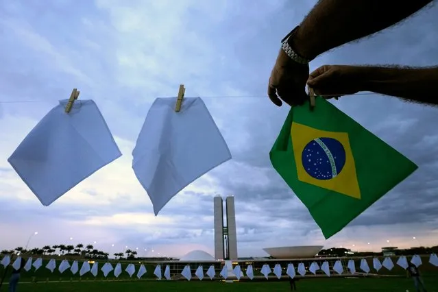 White scarves representing people who have died of COVID-19 in Brazil are hung over a field to protest the government's health policies outside Congress in Brasilia, Brazil, Monday, October 18, 2021. The scarves will be given to members of the Senate Parliamentary Inquiry Commission who are investigating President Jair Bolsonaro's response to the COVID-19 pandemic. (Photo by Eraldo Peres/AP Photo)