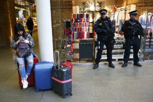A passengers sits on her suitcase as she uses her phone in front of armed police officers on patrol, after Eurostar trains to Brussels were cancelled at St Pancras station in central London, Britain March 22, 2016. (Photo by Andrew Winning/Reuters)