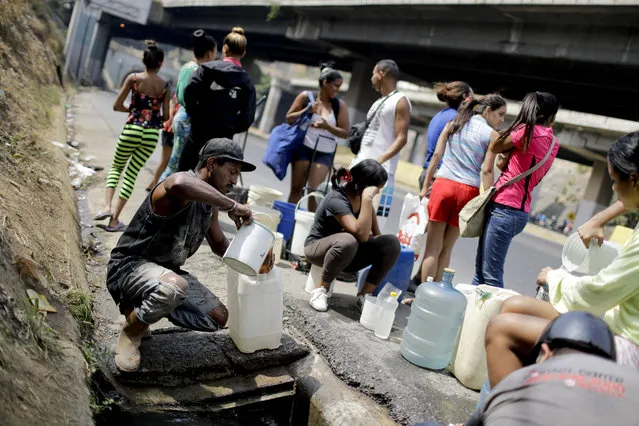 Residents collect water from a ditch next to a highway in Caracas, Venezuela, Tuesday, April 2, 2019. Since a massive power failure struck on March 7, the nation has experienced near-daily blackouts and a breakdown in critical services such as running water and public transportation. (Photo by Natacha Pisarenko/AP Photo)