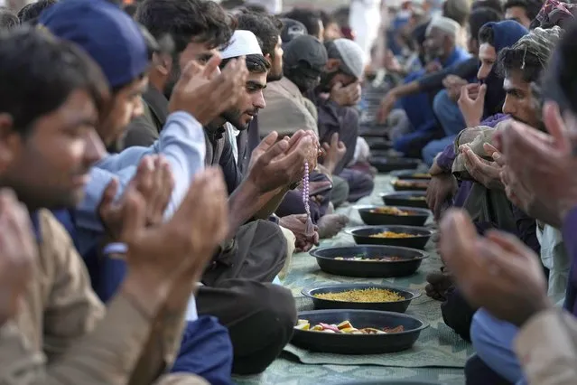 People pray before breaking their fast during the Muslim's holy fasting month of Ramadan, at a free meal distribution point run by a charity group, in Karachi, Pakistan, Wednesday, March 13, 2024. (Photo by Fareed Khan/AP Photo)
