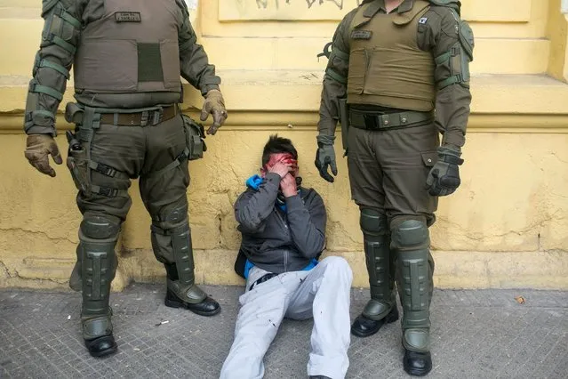 An injured man covers his face after being hit by protesters who accused him of stealing, as riot police stand guard next to him during a demonstration to demand changes in the education system, in Santiago city, May 25, 2015. (Photo by Pablo Sanhueza/Reuters)