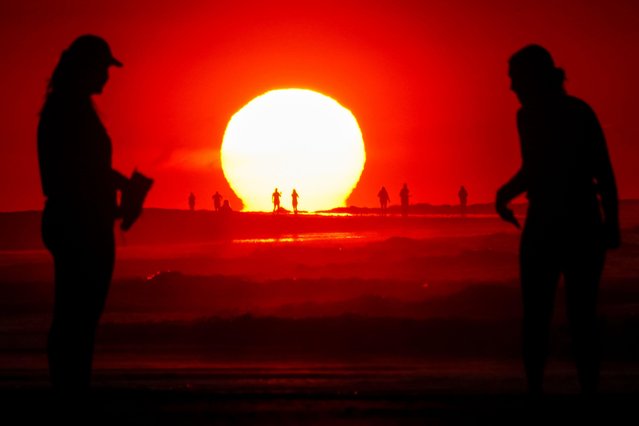 People, silhouetted by a dramatic sunrise, gather along the beach on a clear, hot day, May 16, 2024 in Isle of Palms, South Carolina. (Photo by Richard Ellis/Alamy Live News)