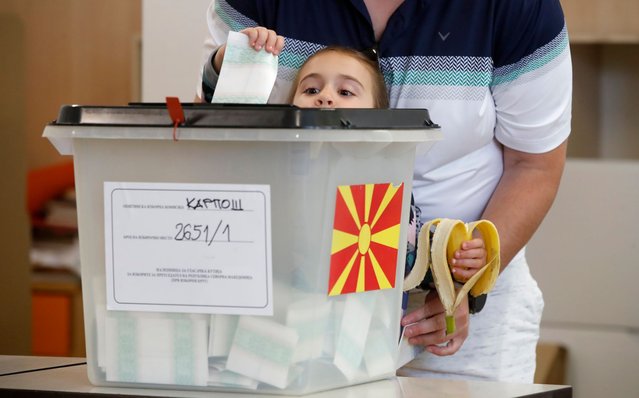 A girl casts the ballot of an adult during the parliamentary election and the presidential runoff, at a polling station in Skopje, North Macedonia, on Wednesday, May 8, 2024. Voters in North Macedonia go to the polls Wednesday for a double election – parliamentary and presidential – following a campaign in which the country's aspirations to join the European Union have played a central role. (Photo by Boris Grdanoski/AP Photo)