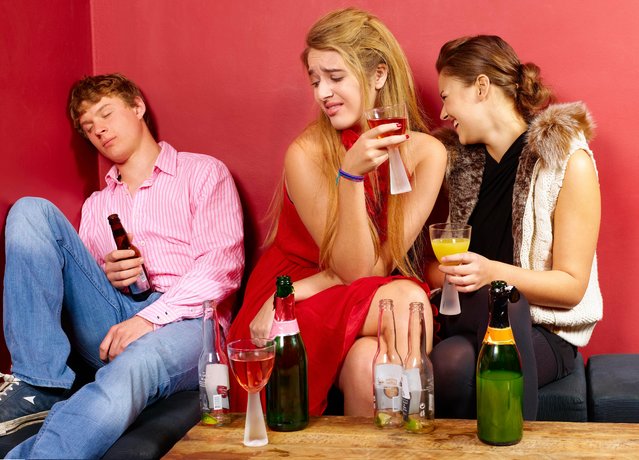 A girl looks with comic disgust at a guy who falls asleep with a bottle of beer at a party; her friend laughs. (Photo by Edward Corbett/Rex Features/Shutterstock)