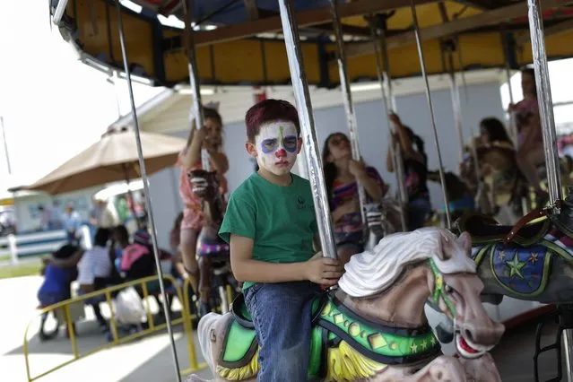 A boy with a painted face rides on a merry-go-round at the Angola Prison Rodeo in Angola, La., Saturday, April 26, 2014. The rodeo got its start in 1965 at a small arena built by a handful of inmates and prison personnel, but it wasn't until 1967 that the rodeo opened to the public. (Photo by Gerald Herbert/AP Photo)