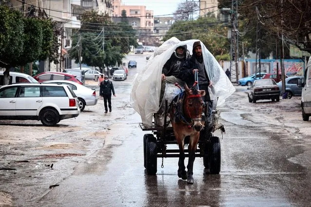 Palestinian men take cover from the rain under a plastic sheet as they ride a donkey-pulled cart in Gaza City, on March 12, 2022. (Photo by Mohammed Abed/AFP Photo)