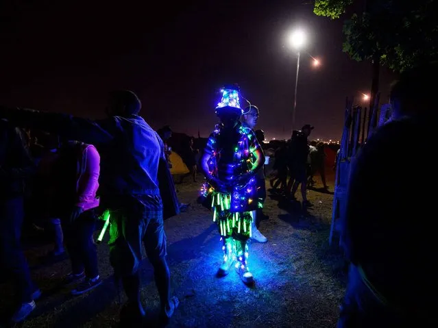A man in a glowing suit walks among festival goers, as revelers gather ahead of this weekends Glastonbury Festival of Music and Performing Arts on Worthy Farm in Somerset. (Photo by Leon Neal/AFP Photo)