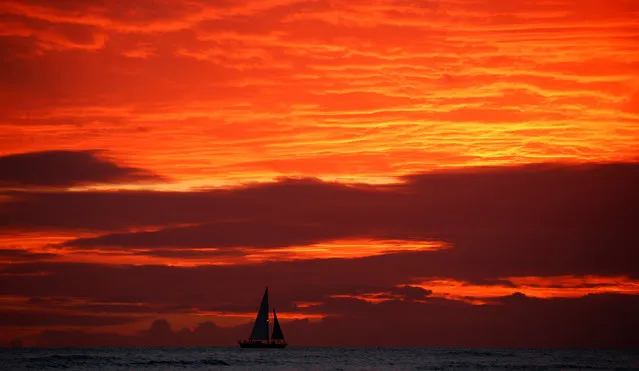 A sailboat passes in front of clouds lit up by the sunset sky off Waikiki in Hawaii, U.S., December 30, 2016. (Photo by Kevin Lamarque/Reuters)