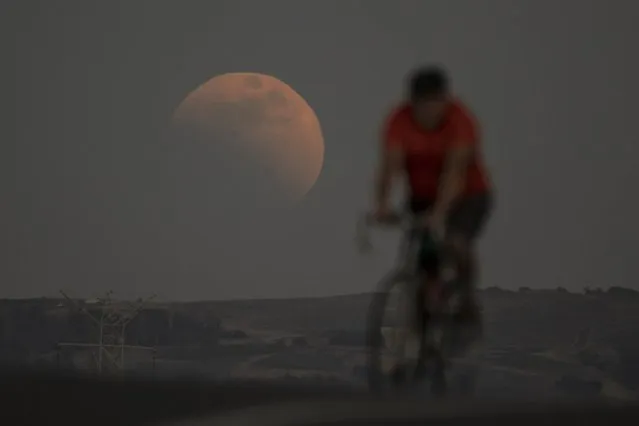 A lunar eclipse is seen behind a cyclist during the first blood moon of the year, in Irwindale, Calif., Sunday, May 15, 2022. (Photo by Ringo H.W. Chiu/AP Photo)