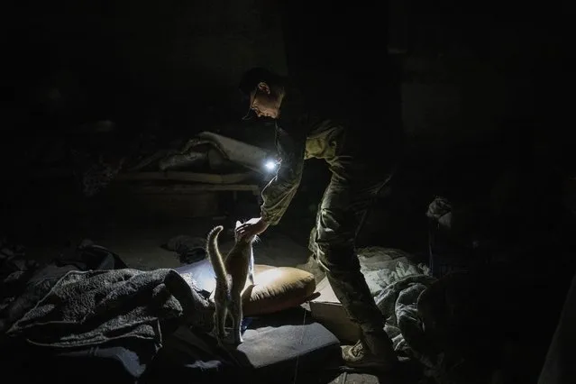 Ukrainian serviceman Anton pets a cat in a basement previously used by Russian soldiers as a temporary base in the village of Malaya Rohan, Kharkiv region, east Ukraine, Monday, May 16, 2022. (Photo by Bernat Armangue/AP Photo)