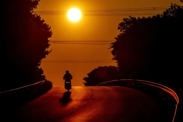 A man rides his scooter over a hill in the outskirts of Frankfurt, Germany, as the sun rises Monday, May 9, 2022. (Photo by Michael Probst/AP Photo)