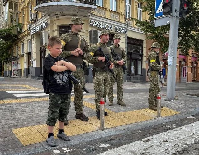 A boy with a toy machine gun stands near Ukrainian servicemen as they patrol an area, amid Russia's attack on Ukraine, in central Kyiv, Ukraine on June 22, 2022. (Photo by Gleb Garanich/Reuters)