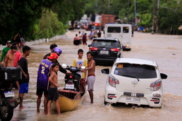 People load a motorcycle onto a wooden boat while vehicles maneuver through a flooded highway caused by heavy rains brought about by Tropical Storm Trami, in Nabua town, Camarines Sur province on October 23, 2024. Torrential rains driven by the storm have turned streets into rivers, submerged entire villages and buried some vehicles up to their door handles in volcanic sediment knocked loose by the downpour. (Photo by Charism Sayat/AFP Photo)