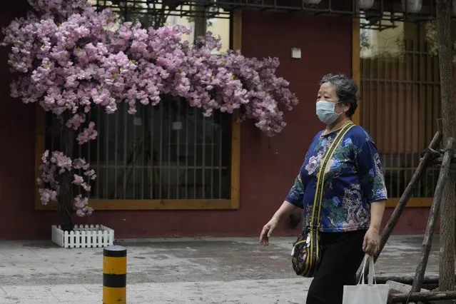 A woman wearing a mask walks past plastic flower decorations, Wednesday, July 6, 2022, in Beijing. (Photo by Ng Han Guan/AP Photo)