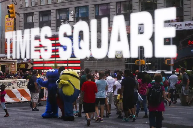 A person dressed as the Sesame Street character Cookie Monster (L) and “Minion” from the “Despicable Me” movie are reflected in a window as they attempt to attract customers to pose for photos and tips in Times Square in New York July 29, 2014. (Photo by Eduardo Munoz/Reuters)