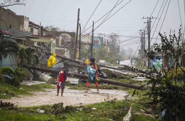 Residents walk near downed power lines felled by Hurricane Irma, in Caibarien, Cuba, Saturday, September 9, 2017. There were no reports of deaths or injuries after heavy rain and winds from Irma lashed northeastern Cuba. Seawater surged three blocks inland in Caibarien. (Photo by Desmond Boylan/AP Photo)