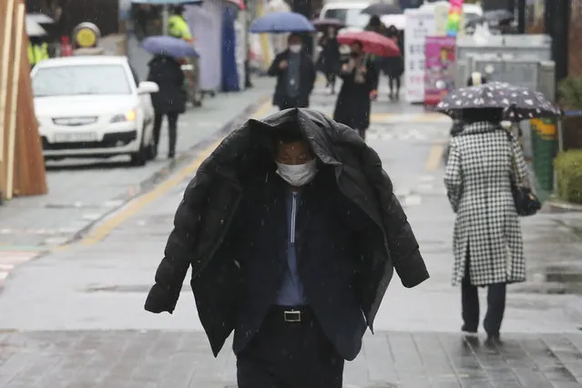 A man wearing a face mask walks in the rain on a street in Seoul, South Korea, Tuesday, March 10, 2020. For most people, the new coronavirus causes only mild or moderate symptoms, such as fever and cough. For some, especially older adults and people with existing health problems, it can cause more severe illness, including pneumonia. (Photo by Ahn Young-joon/AP Photo)