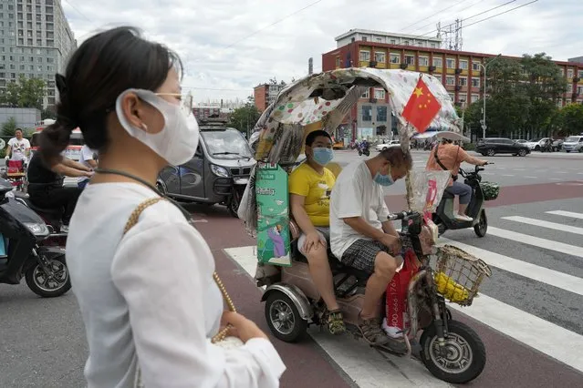 A man and a child wearing masks sit in an electric tricycle with a Chinese national flag in Beijing, Monday, August 15, 2022. (Photo by Ng Han Guan/AP Photo)