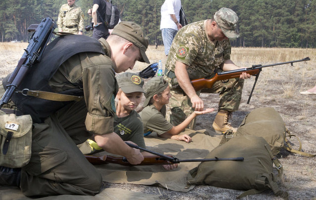 Servicemen teach children to shoot with a rifle at a military training ground of Ukraine's National Guard outside the village of Stare, the Kiev region, Ukraine, Saturday, August 29, 2015. (Photo by Efrem Lukatsky/AP Photo)