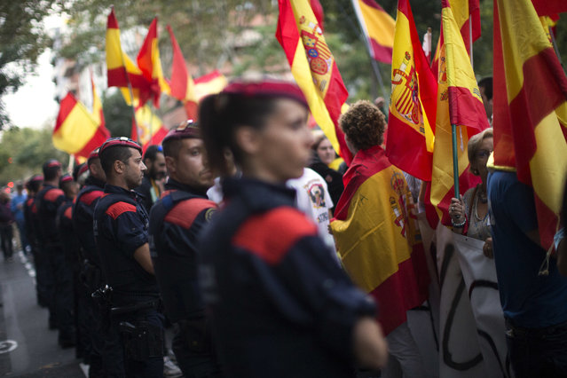 In this Friday, September 22, 2017 photo, Mossos d'Esquadra police officers cordon off the area as right wing demonstrators hold Spanish flags during a protest against the Oct. 1 vote, in Barcelona, Spain. (Photo by Emilio Morenatti/AP Photo)