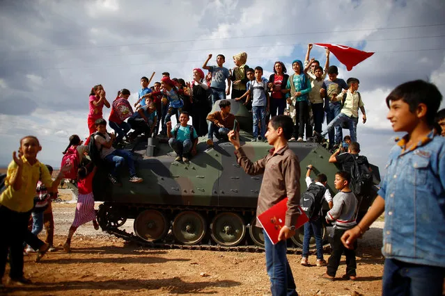 Children stand on top of a Turkish Armed Forces vehicle, as a military convoy pass by their village on the Turkish-Syrian border line in Reyhanli, Hatay province, Turkey on October 12, 2017. (Photo by Osman Orsal/Reuters)