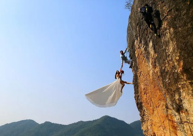 Zheng Feng, an amateur climber takes wedding pictures with his bride on a cliff in Jinhua, Zhejiang province, October 26, 2014. (Photo by Reuters/China Daily)