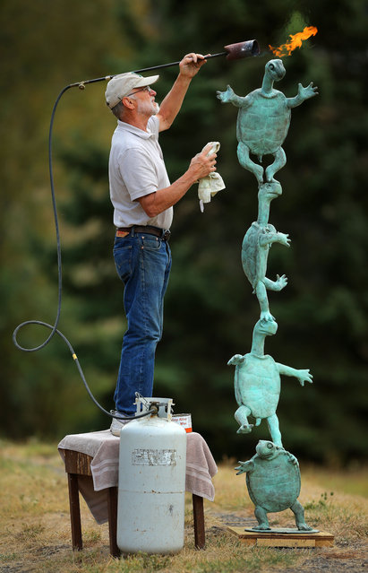 In this photo taken on Monday, September 22, 2014, artist Peter Helzer puts the finishing touches on his whimsical turtle sculpture at his Dexter, Ore. home and studio. The quartet of balancing turtles has been the centerpiece of “Turtle Plaza” at the Oregon Zoo in Portland since 1989. (Photo by Brian Davies/AP Photo/The Register-Guard)