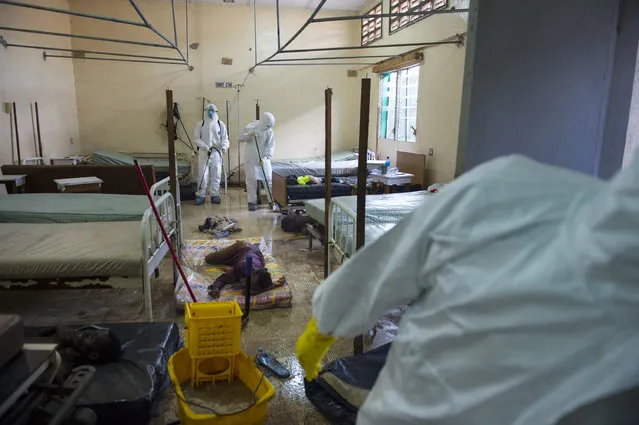 Hospital workers clean a ward while a woman is still on a mattress on the floor the Redemption  Hospital which has become a transfer and holding center to intake Ebola patients located in one of the poorest neighborhoods of Monrovia that locals call “New Kru Town” on Saturday September 20, 2014 in Monrovia, Liberia. (Photo by Michel du Cille/The Washington Post)