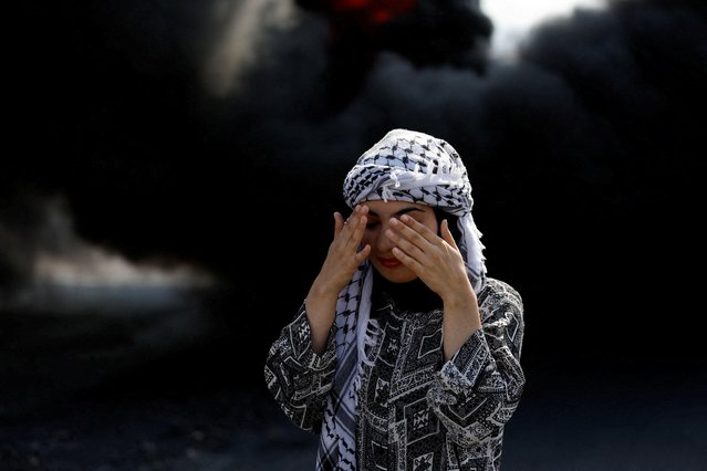 A Palestinian demonstrator reacts as smoke rises from a burning tire during a protest demanding Israel to reopen closed roads leading to Nablus, at the Hawara checkpoint near Nablus in the Israeli-occupied West Bank on November 1, 2022. (Photo by Mohamad Torokman/Reuters)