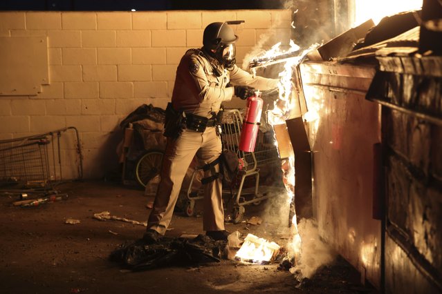 A law enforcement officer works to put out a fire during a protest in Compton, Calif., Saturday, June 7, 2025, after federal immigration authorities conducted operations. (Photo by Ethan Swope/AP Photo)