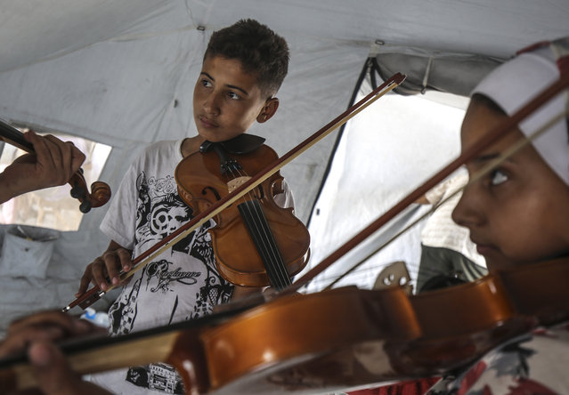 Volunteer teachers provide lessons in oud, violin, and darbuka to children displaced by Israel's ongoing attacks since October 7, 2023, helping them temporarily forget the negative effects of the conflict in the Gaza Strip on June 4, 2025. The lessons take place at a temporary music school established in a tent camp. Living under difficult conditions, the children are introduced to music amid the tents, offering a brief respite. (Photo by Mahmoud Issa/Anadolu via Getty Images)