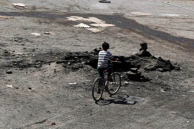 A boy rides a bicycle near a hole in the ground after an airstrike on Sunday in the rebel-held town of Dael, in Deraa Governorate, Syria September 19, 2016. (Photo by Alaa Al-Faqir/Reuters)