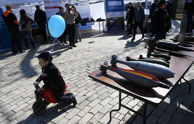 A child rides a scooter past a display of shells during an open-air information day in the centre of Kiev on April 4, 2018, marking International Mine Awareness Day. More than 1,800 people have been affected by mines and explosive devices and more than 600 of them have died, including children, said Deputy Minister of Foreign Affairs of Ukraine Vasily Bodnar during the event opening. According to international experts, it will take another 10-15 years and millions of investments to complete total clearance of the country's war-torn east, he added. (Photo by Sergei Supinsky/AFP Photo)
