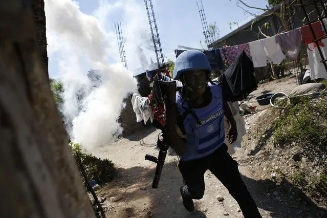 A U.N. peacekeeper from Senegal runs after throwing a tear gas grenade as security forces clash with rock-throwing neighborhood residents outside a U.N. base in Les Cayes, Haiti, Saturday, October 15, 2016. (Photo by Rebecca Blackwell/AP Photo)