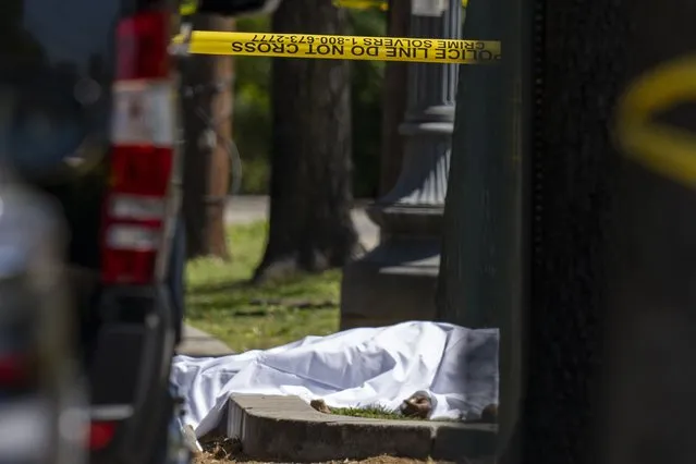 A victim lies under a sheet as Metropolitan Police Department officers investigate the shooting scene in front of Stewart Funeral Home, Tuesday, April 11, 2023, in Washington. Police say a man was killed and three others were critically injured in a shooting outside of a funeral for a homicide victim in the nation’s capital.(Photo by Alex Brandon/AP Photo)
