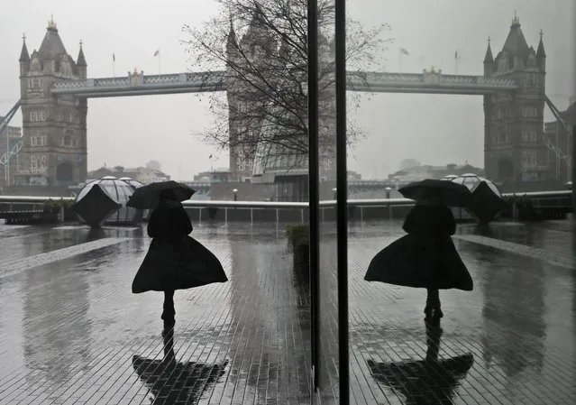 A woman is reflected in a window as she braves wind and rain while walking towards Tower Bridge in London, Thursday, January 14, 2021 during England's third national lockdown to curb the spread of coronavirus. (Photo by Kirsty Wigglesworth/AP Photo)