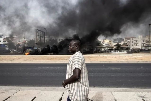 A man passes by a smoke billowing from burning tyres during a protest in Dakar on May 29, 2023, over the arrest of opposition leader Ousmane Sonko ahead of the final verdict in his rape trial. Sonko, who has a significant youth following, is facing a rape trial which could result in him being ineligible to run in next year's presidential election. (Photo by John Wessels/AFP Photo)