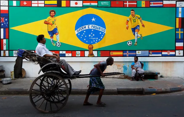 A rickshaw puller transports a passenger past a mural depicting Brazil's Neymar and Marcelo, ahead of the FIFA World Cup, along a street in Kolkata, India June 14, 2018. (Photo by Rupak De Chowdhuri/Reuters)
