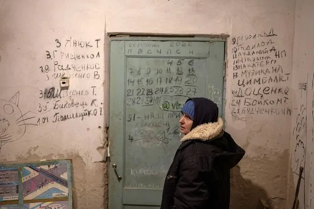 Halyna Tolochina stands in front of a wall inscribed with the names of people who died inside a school basement, as Russia's invasion of Ukraine continues, in the village of Yahidne, near to Chernihiv, Ukraine on April 6, 2022. Tolochina, a member of the village council, struggled to compose herself as she went through the list, scribbled in black on the plaster either side of a green door. To the left of the door were scrawled the seven names of people killed by Russian soldiers. To the right were the 10 names of people who died because of the harsh conditions in the basement, she said.  “This old man died first”, Tolochina said, pointing at the name of Muzyka D., for Dmytro Muzyka, whose death was recorded on March 9. “He died in the big room, in this one”. (Photo by Marko Djurica/Reuters)